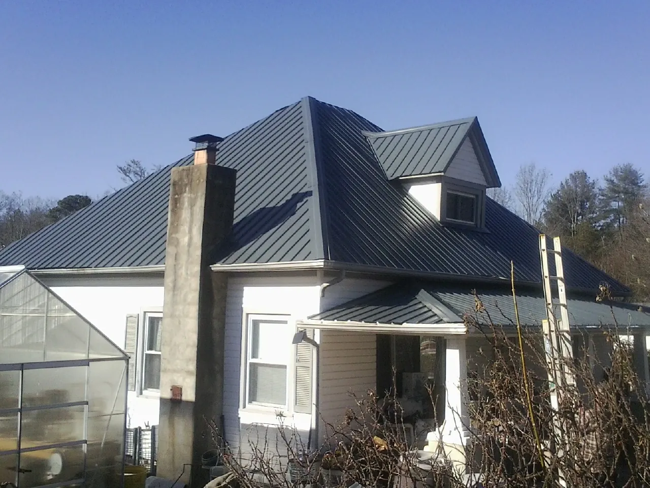 Dark blue standing seam metal roof on a white farmhouse with dormer — Slate & Tile Roof Repair by Roofing Brothers in Carmel