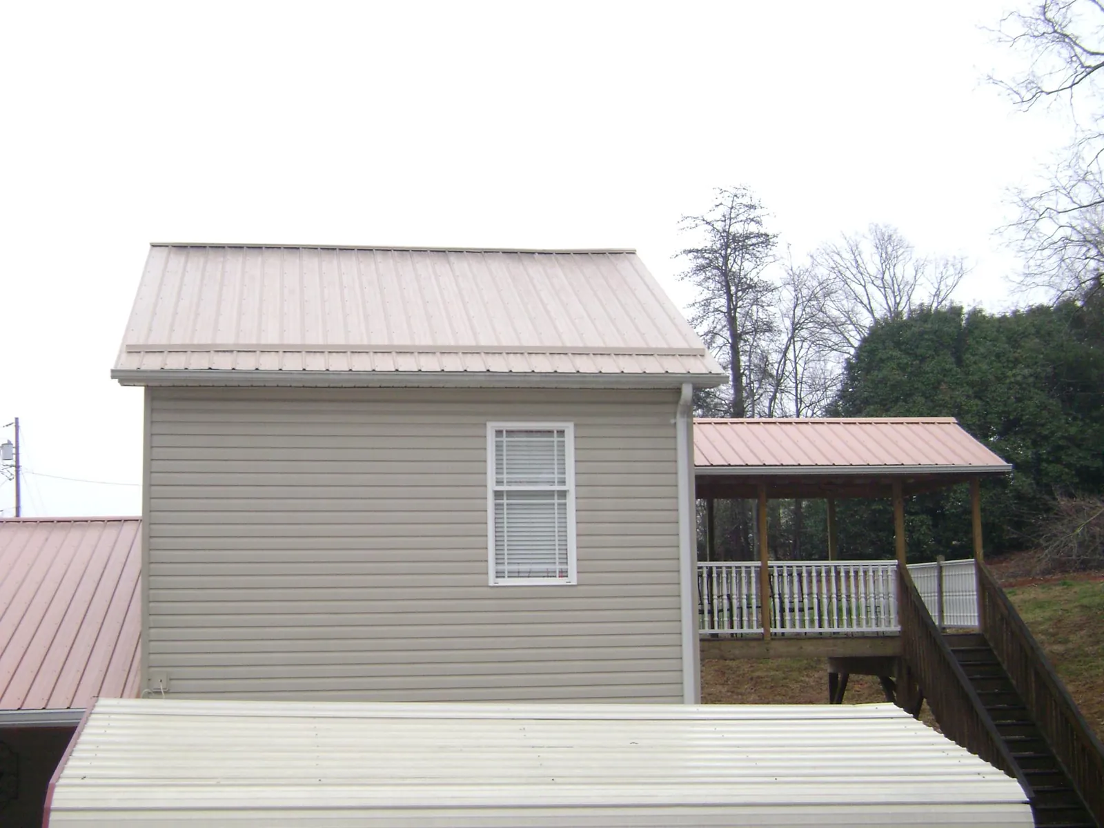 Tan metal roofs on a two story addition and attached porch, from a Roof Replacement job in Carmel